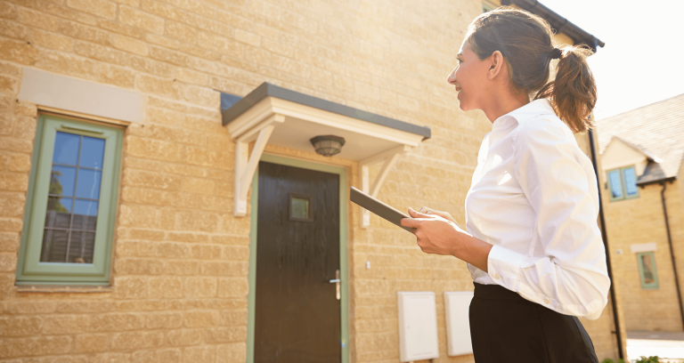 A woman surveying a house and taking notes